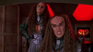 Two Klingon warriors in metallic armor stand in a red-lit sci‑fi set, one snarling toward the camera and showing teeth.